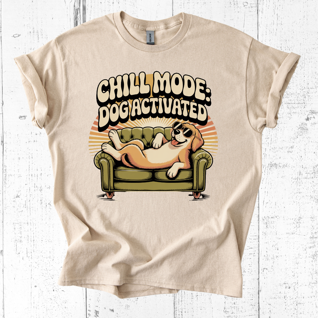 Beige t-shirt with a graphic of a dog on a couch and text 'Chill Mode: Dog Activated' on a white wooden background.