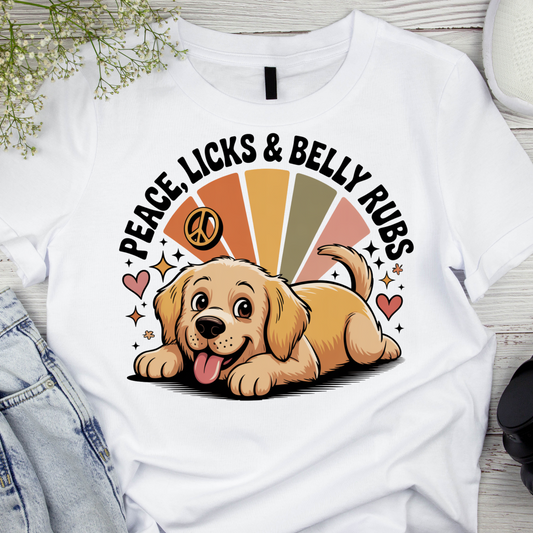 White t-shirt with a cartoon dog and text 'Peace, Licks & Belly Rubs' on a wooden surface.