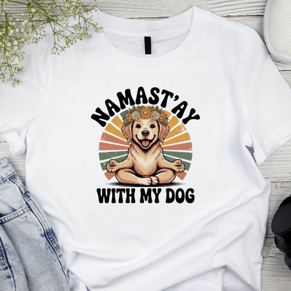 White t-shirt with a dog graphic and text 'Namast'ay with my dog' on a wooden surface.