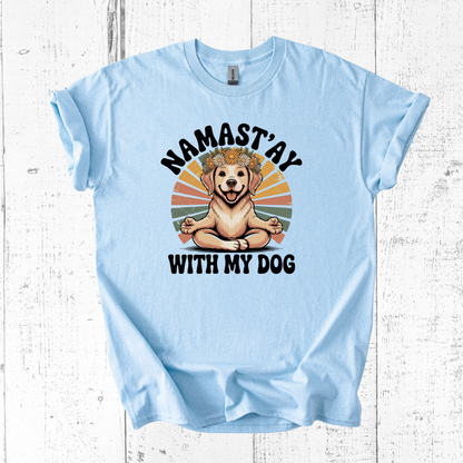 Light blue t-shirt with a dog graphic and text 'Namast'ay with my dog' on a wooden surface.