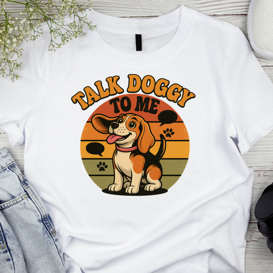 White t-shirt with a dog graphic and 'Talk Doggy to Me' text on a wooden surface.