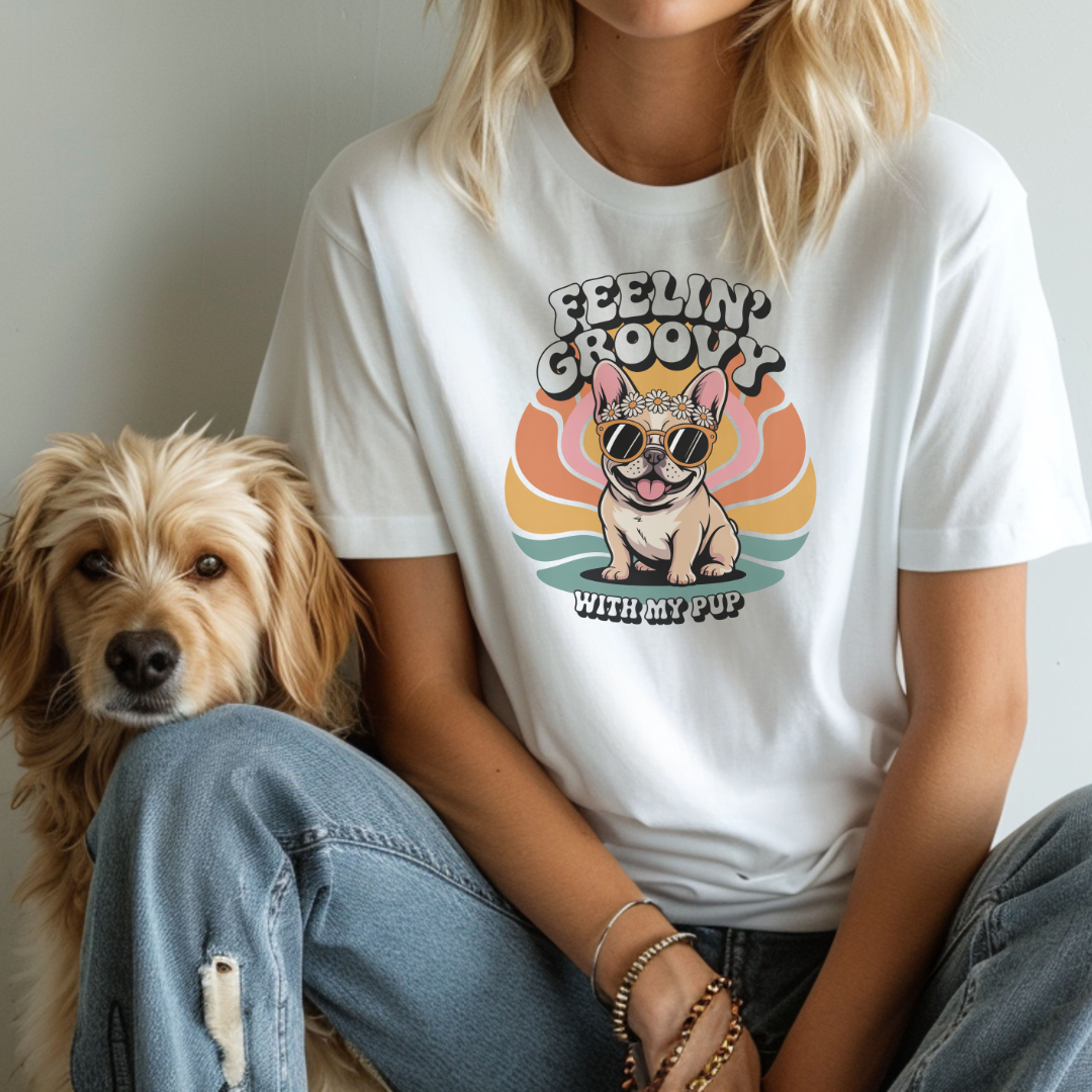 Person wearing a white t-shirt with a dog graphic and 'Feelin' Groovy with my pup' text, sitting next to a dog.