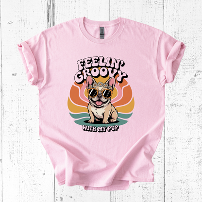 Pink t-shirt with a dog graphic and 'Feelin' Groovy with my Pup' text on a white wooden background