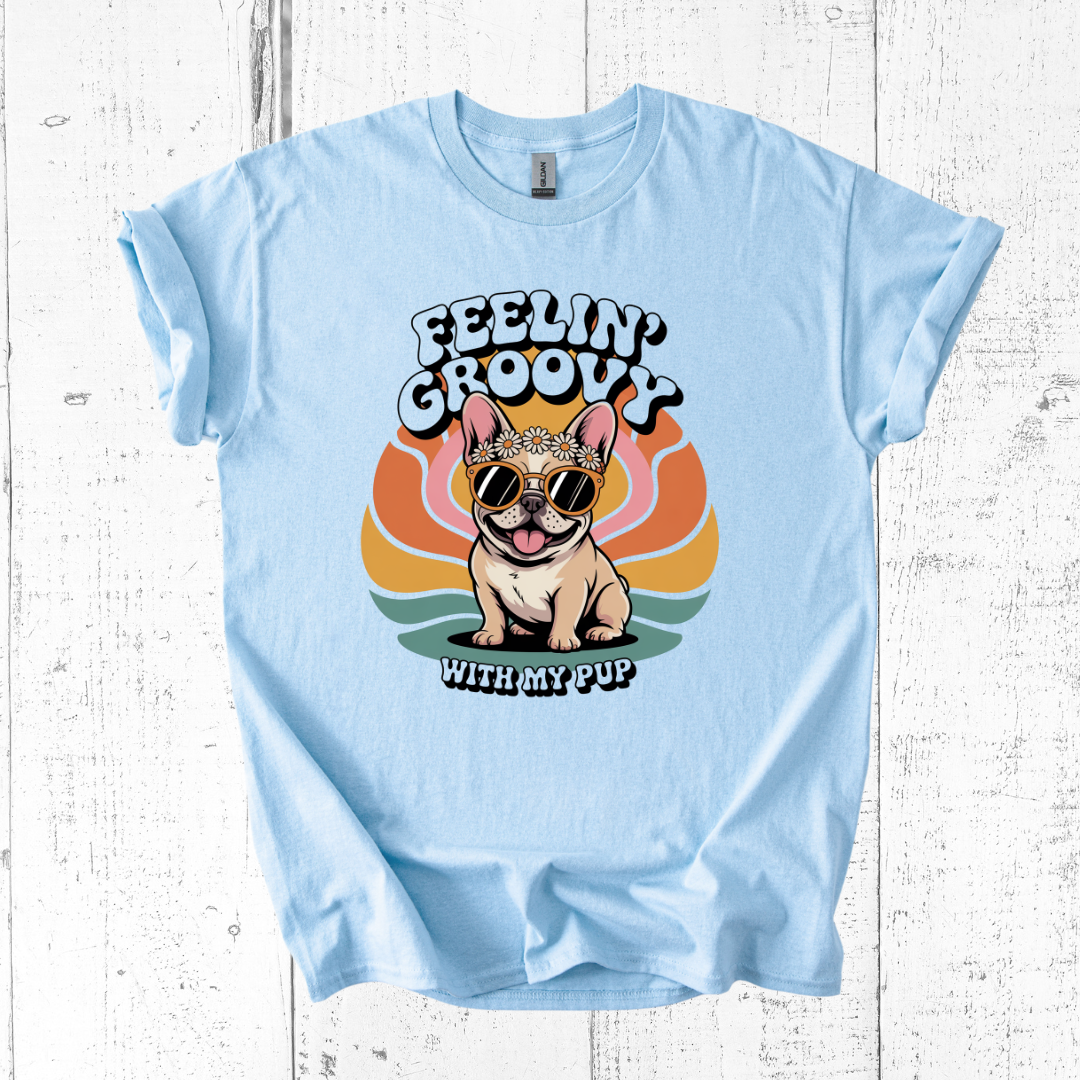 Light blue t-shirt with a dog graphic and 'Feelin' Groovy with my pup' text on a wooden surface.