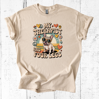 Beige t-shirt with a graphic of a dog and text 'My therapist has four legs' on a white wooden background