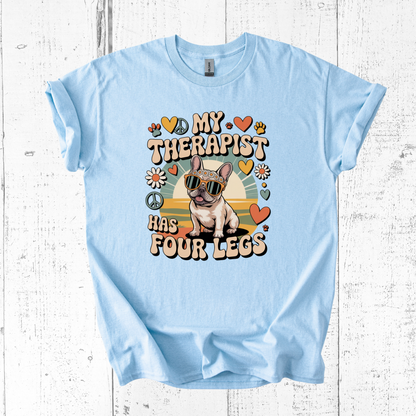 Light blue t-shirt with a graphic of a dog and text 'My therapist has four legs' on a white wooden background.