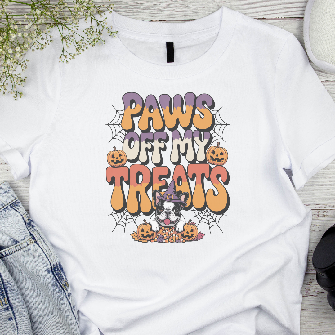 White t-shirt with Halloween-themed design featuring text 'Paws Off My Treats' and pumpkins on a wooden surface.