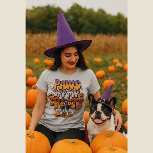 Woman wearing a Halloween-themed shirt and purple witch hat with a dog in a pumpkin patch.