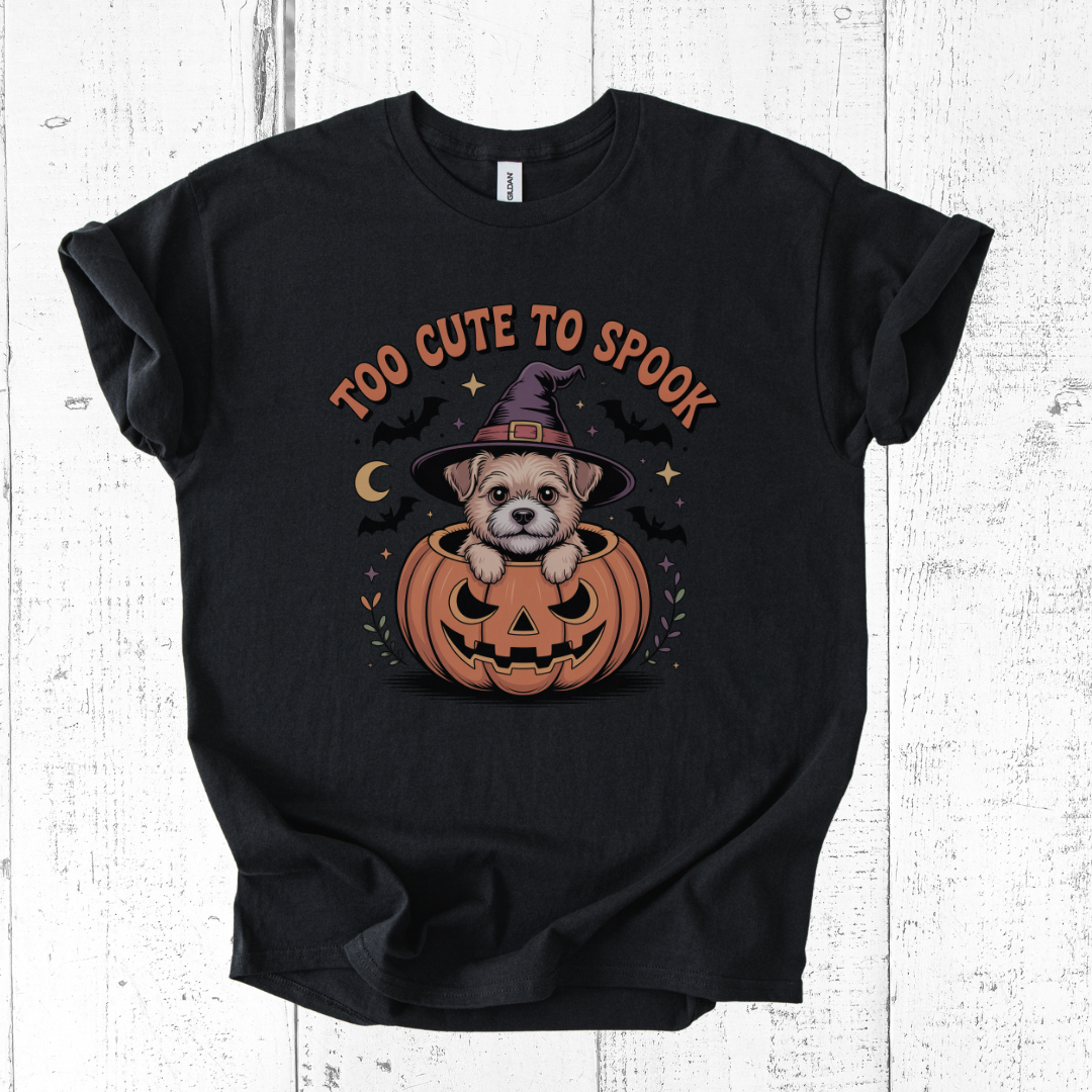 Black t-shirt with Halloween design of a dog in a pumpkin and 'Too Cute To Spook' text on a white wooden background.
