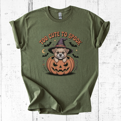 Green t-shirt with a Halloween-themed design of a dog in a pumpkin, text 'Too Cute to Spook', on a white wooden background.