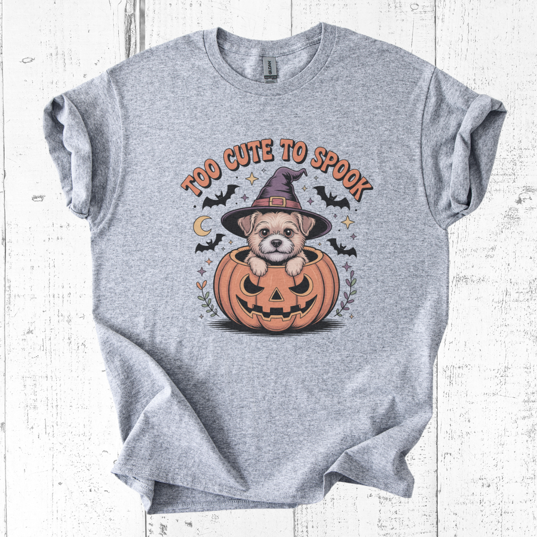 Gray t-shirt with a Halloween design of a dog in a pumpkin and 'Too Cute To Spook' text on a white wooden background.