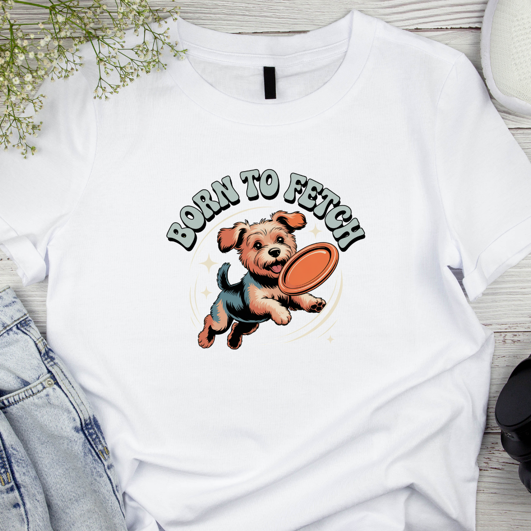 White t-shirt with a dog graphic and 'Born to Fetch' text on a wooden surface.