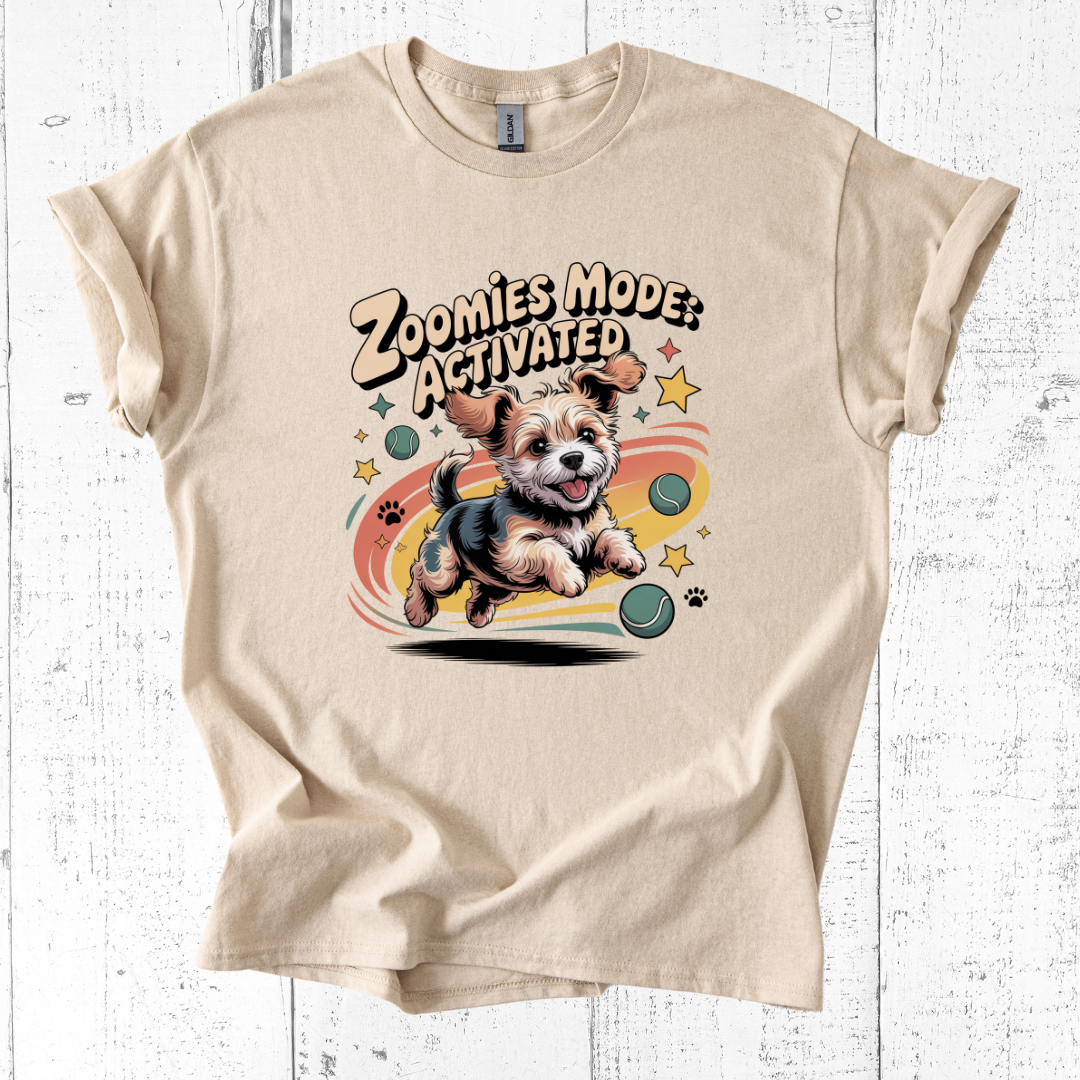 Beige t-shirt with a dog graphic and 'Zoomies Mode Activated' text on a white wooden background