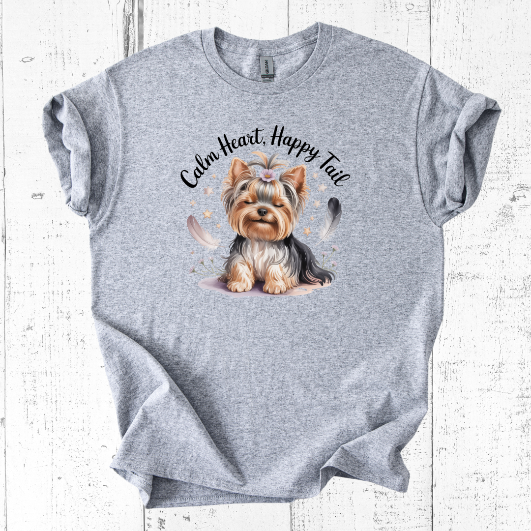 Gray t-shirt with a dog illustration and 'Calm Heart, Happy Tail' text on a wooden surface
