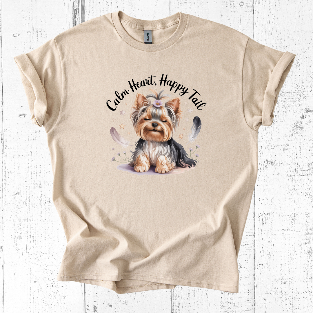 Beige t-shirt with a dog illustration and 'Calm Heart, Happy Tail' text on a wooden surface