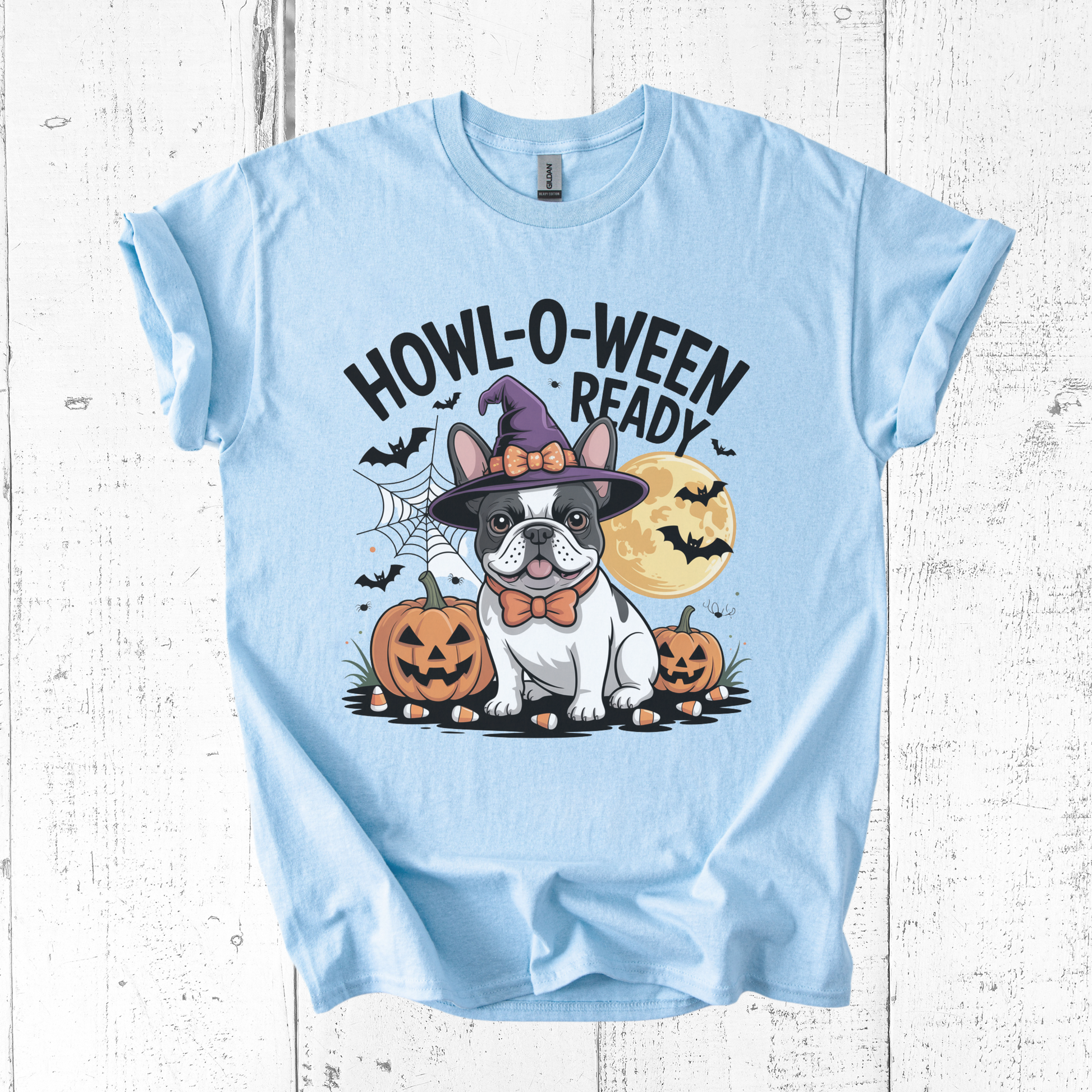 Light blue t-shirt with Halloween-themed design featuring a dog in a witch hat and pumpkins on a white wooden background.