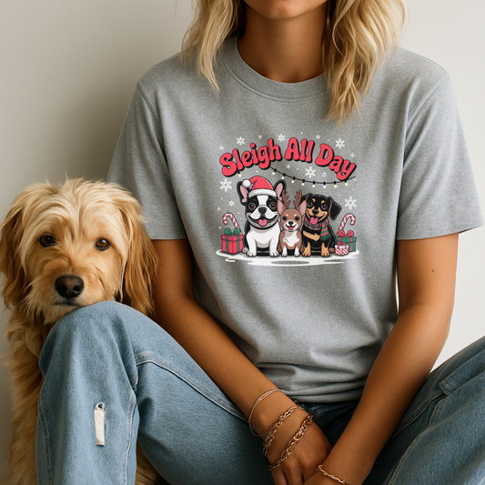 Person wearing a gray t-shirt with a dog graphic and 'Sleigh All Day' text, sitting next to a dog.
