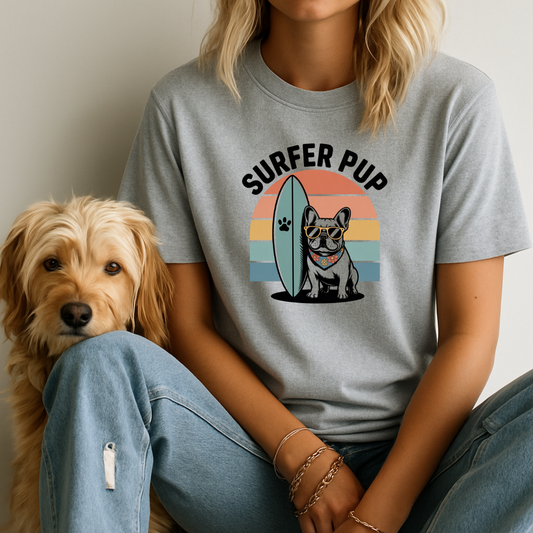 Person wearing a 'Surfer Pup' t-shirt with a dog graphic, sitting next to a dog.