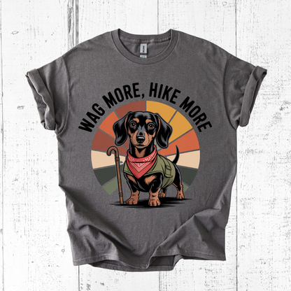 Gray t-shirt with a dachshund graphic and 'Wag More, Hike More' text on a white wooden background