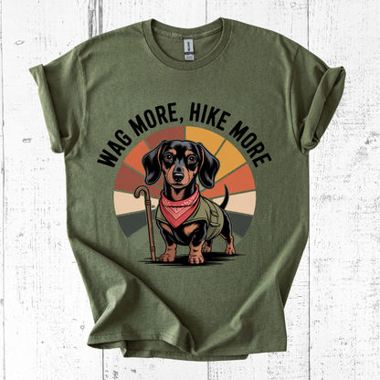 Green t-shirt with a dachshund graphic and 'Wag More, Hike More' text on a white wooden background