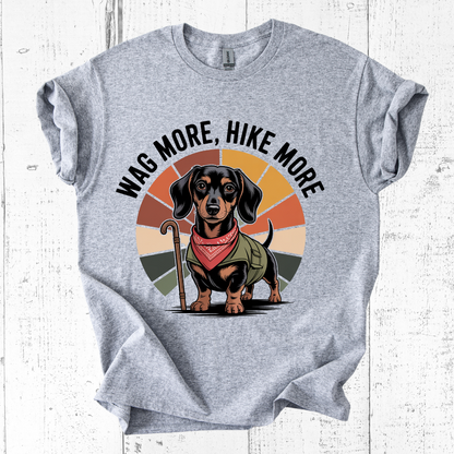 Gray t-shirt with a dachshund graphic and 'Wag More, Hike More' text on a white wooden background