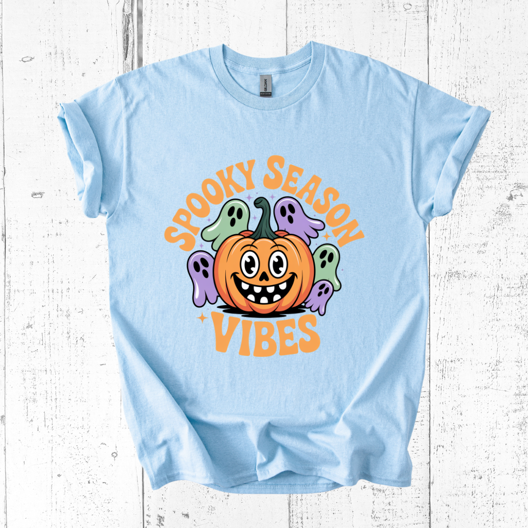 Light blue t-shirt with Halloween-themed design featuring a pumpkin and ghosts on a white wooden background.