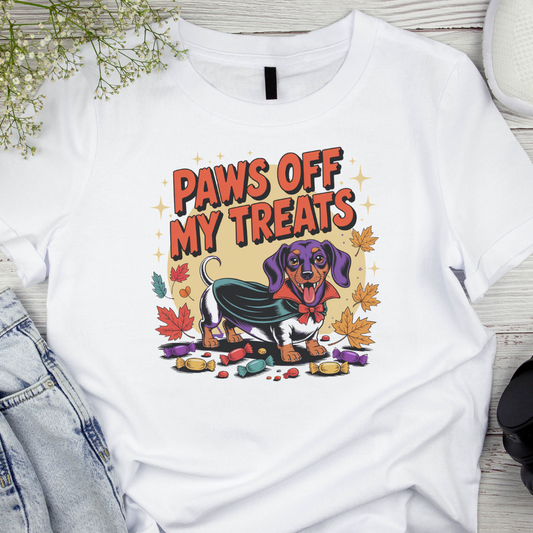 White t-shirt with a graphic of a dog and text 'Paws Off My Treats' on a wooden surface.