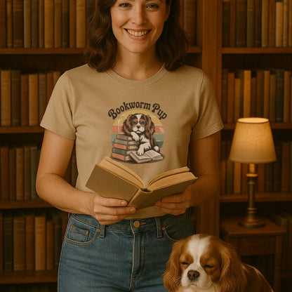 Woman wearing a 'Bookworm Pup' t-shirt holding a book with a dog in front of a bookshelf.