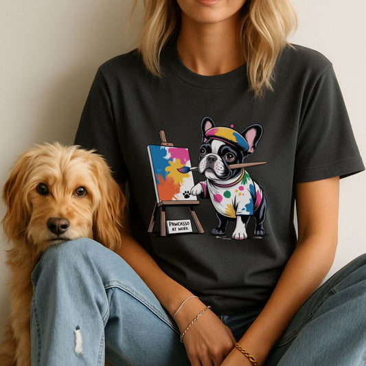 Person wearing a black t-shirt with a colorful dog painting design, sitting next to a dog.