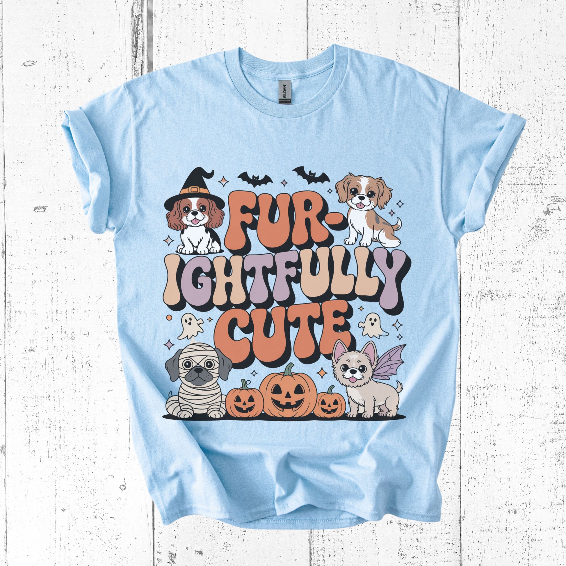 Light blue t-shirt with Halloween-themed graphic of dogs and text on a wooden surface
