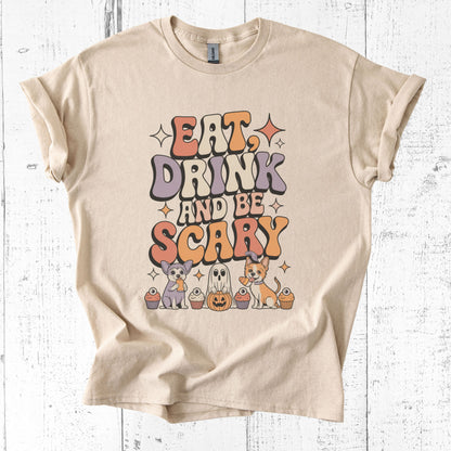 Beige t-shirt with Halloween-themed graphic and text 'Eat, Drink and Be Scary' on a white wooden background.
