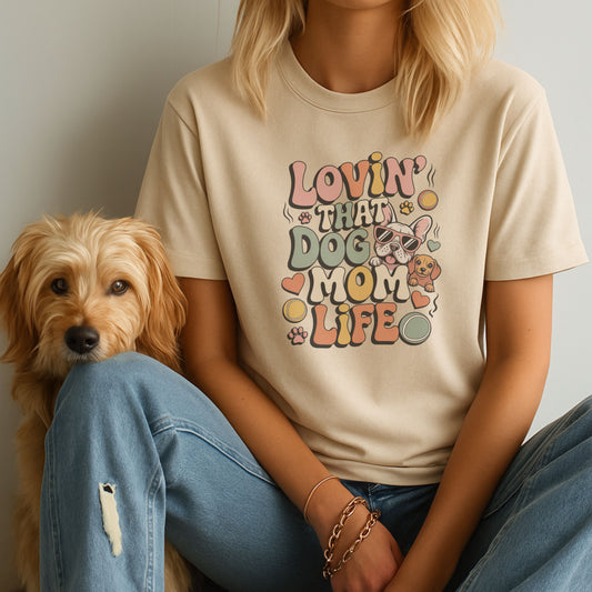 Person wearing a 'Lovin' That Dog Mom Life' t-shirt sitting next to a dog.