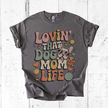 Gray t-shirt with colorful 'Lovin' That Dog Mom Life' graphic on a white wooden surface