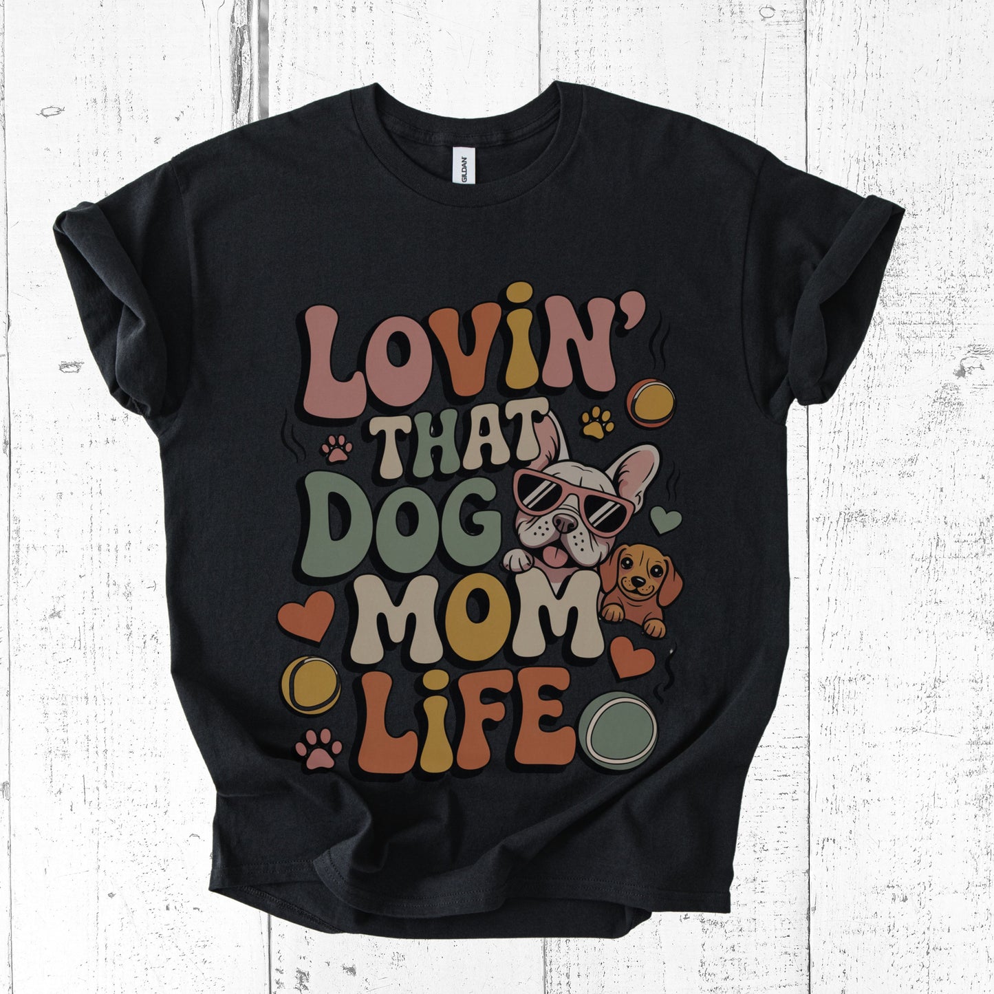 Black t-shirt with colorful graphic and text 'Lovin' That Dog Mom Life' on a white wooden background