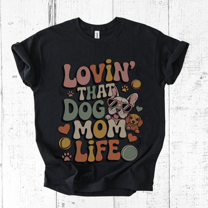 Black t-shirt with colorful graphic and text 'Lovin' That Dog Mom Life' on a white wooden background