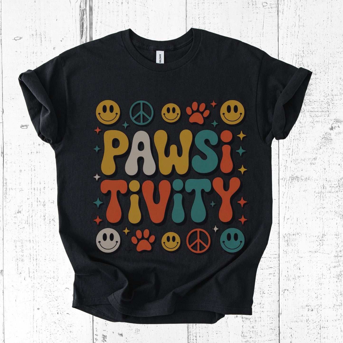 Black t-shirt with colorful 'PAWSI TIVITY' design on a white wooden background