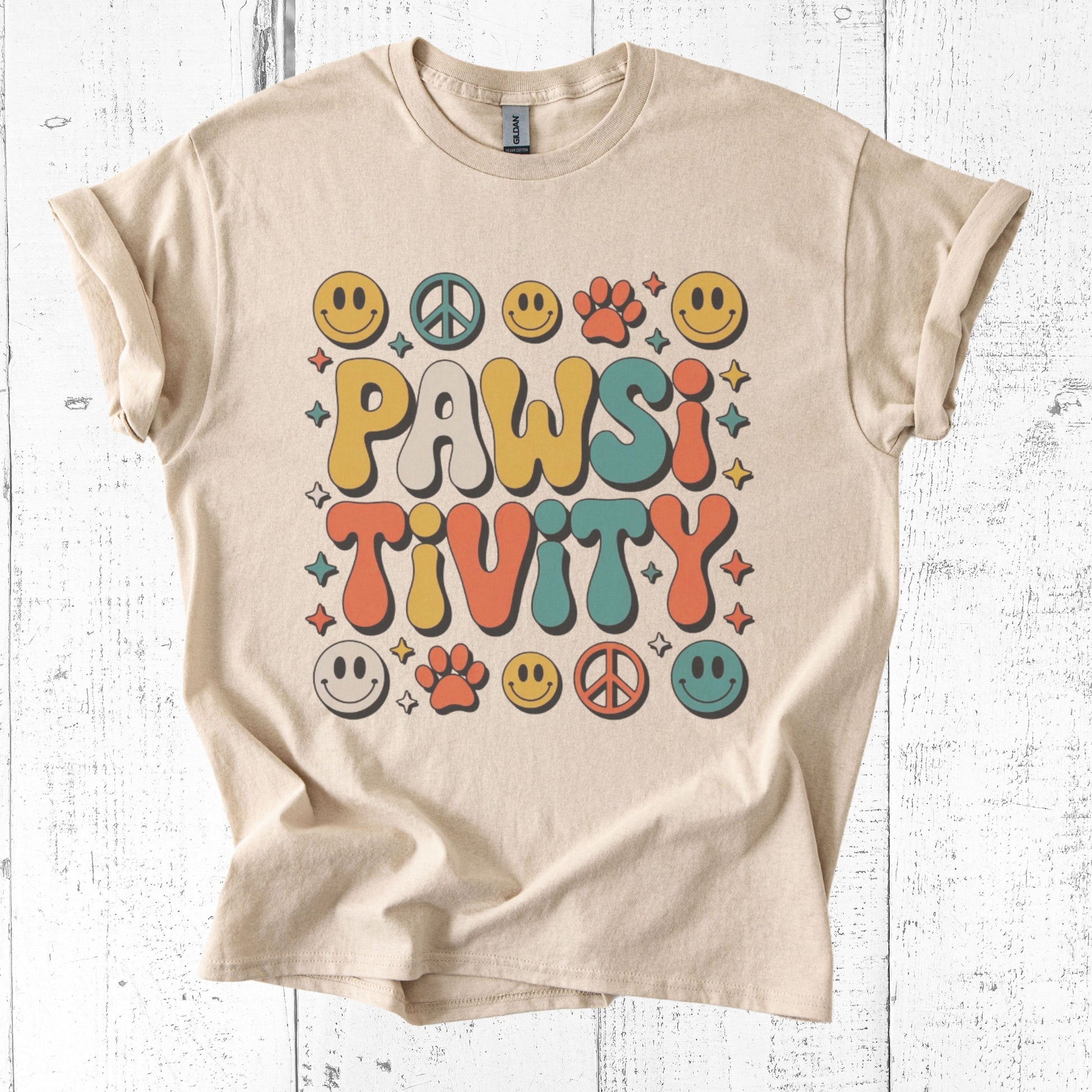 Beige t-shirt with 'PAWSITIVITY' design on a white wooden background