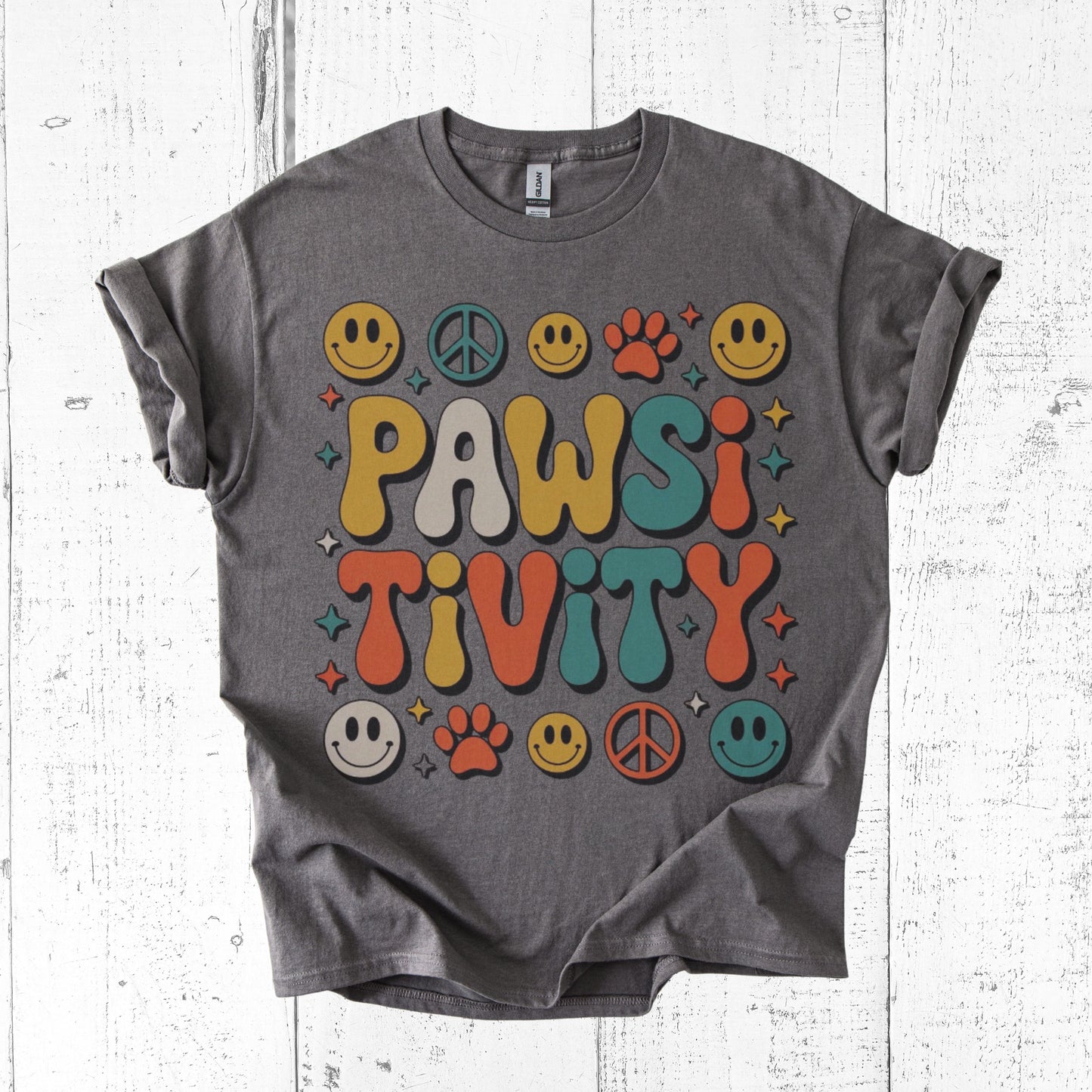 Gray t-shirt with colorful 'PAWSI TIVITY' design on a white wooden surface
