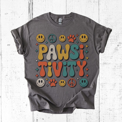 Gray t-shirt with colorful 'PAWSI TIVITY' design on a white wooden surface