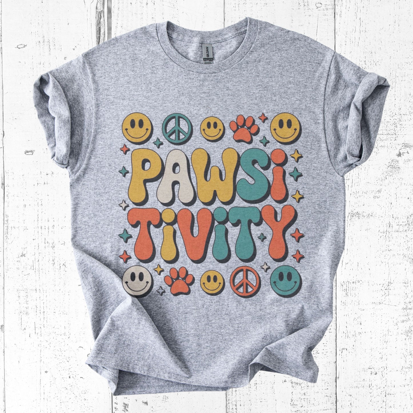 Gray t-shirt with colorful 'PAWSITIVITY' design on a white wooden background