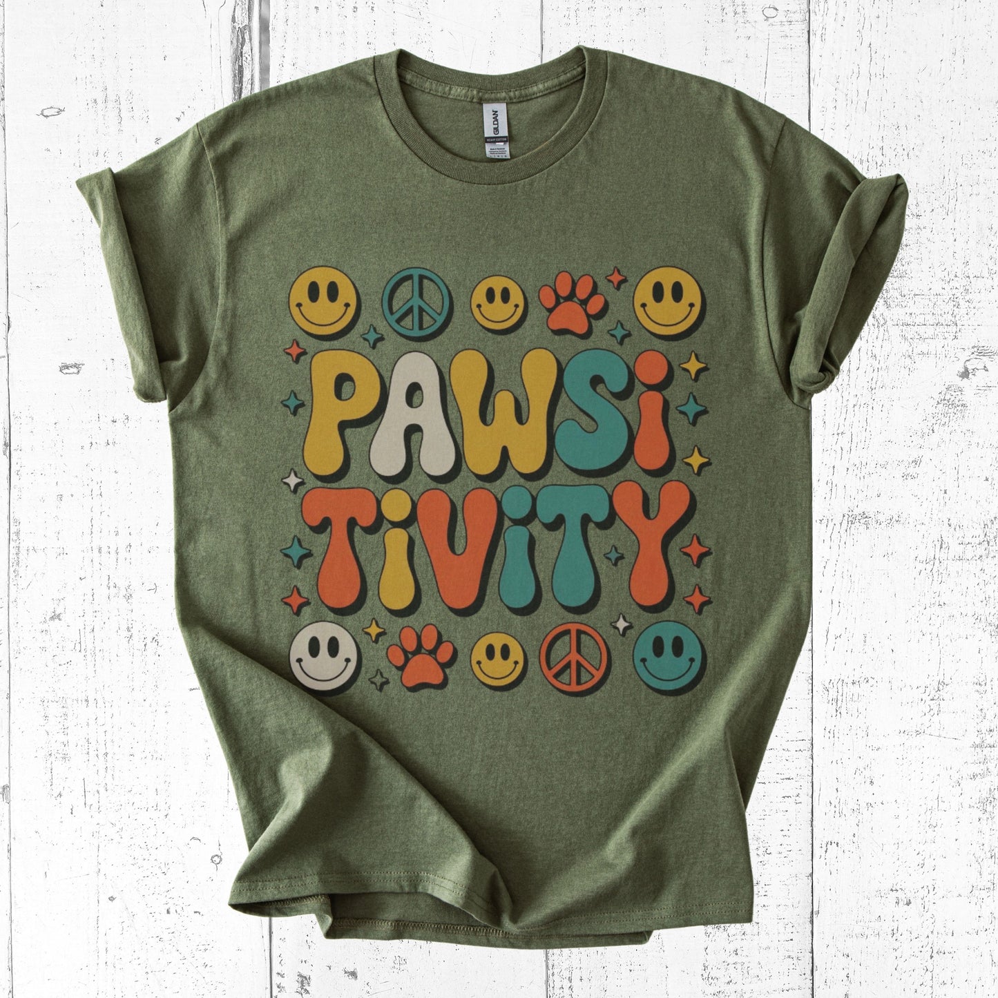 Green t-shirt with colorful 'PAWSITIVITY' design on a white wooden background