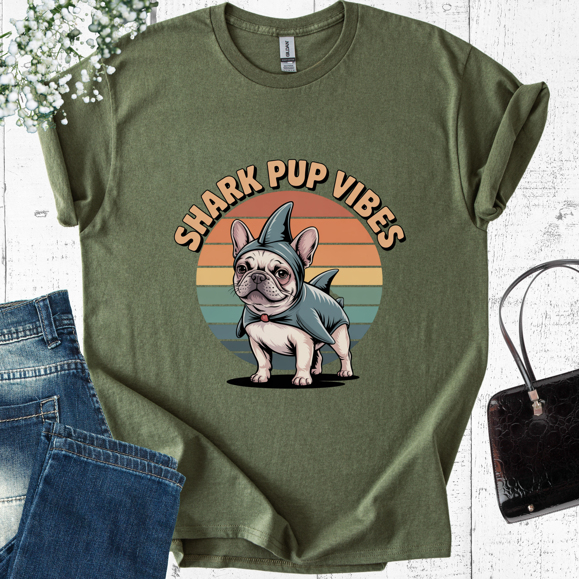 Green t-shirt with a dog in a shark costume graphic and 'Shark Pup Vibes' text, placed on a white surface with jeans and a handbag.