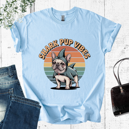 Light blue t-shirt with a graphic of a dog in a shark costume and 'Shark Pup Vibes' text on a wooden surface.