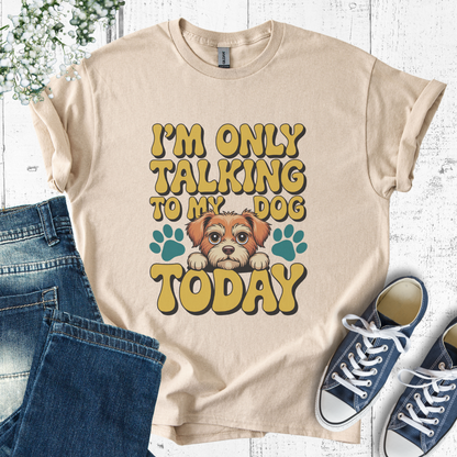 Beige t-shirt with a dog graphic and text, paired with jeans and sneakers on a light wooden background.