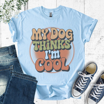 Light blue t-shirt with 'My Dog Thinks I'm Cool' text, paired with jeans and sneakers on a wooden surface.