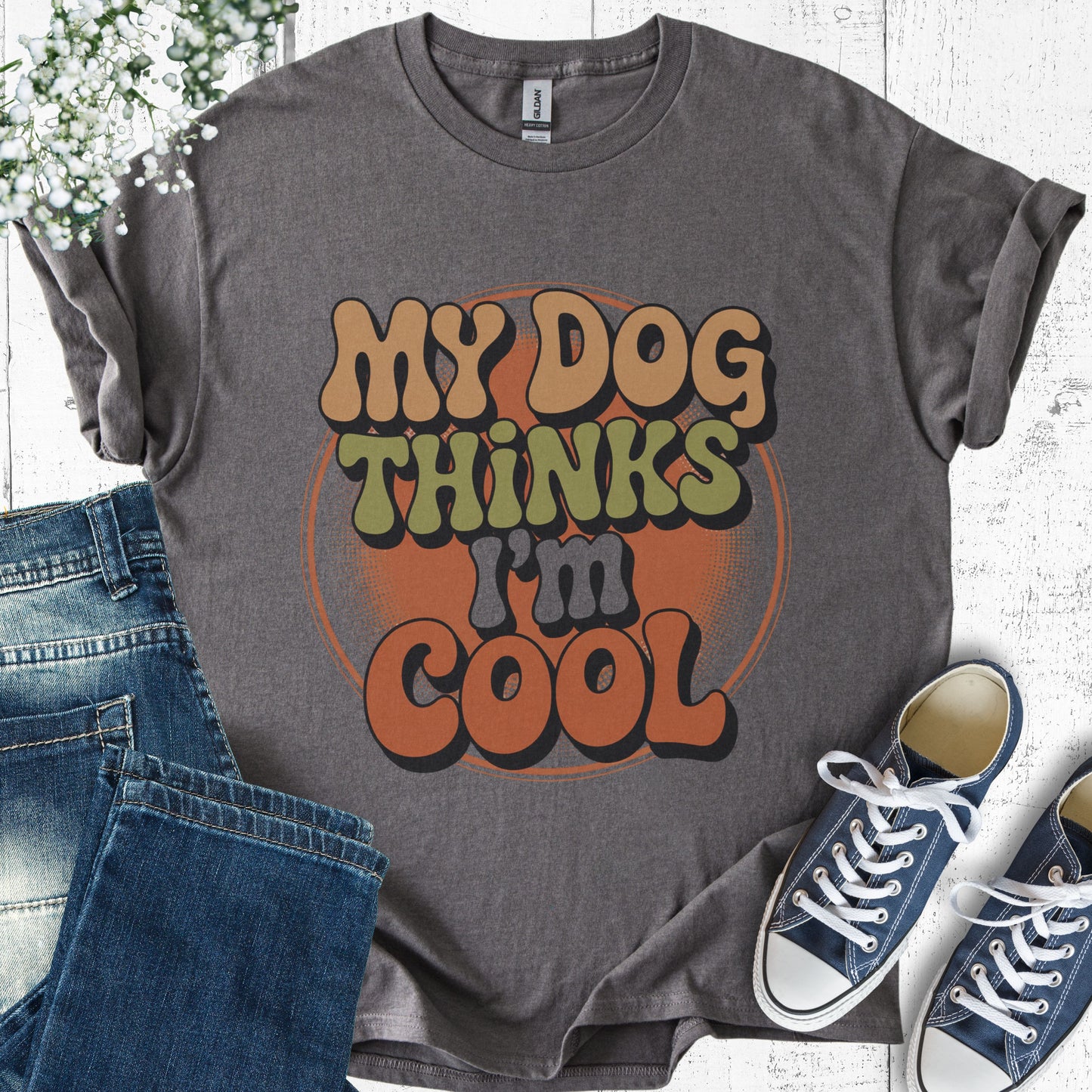 Gray t-shirt with 'My Dog Thinks I'm Cool' text, paired with jeans and sneakers on a light wooden surface.