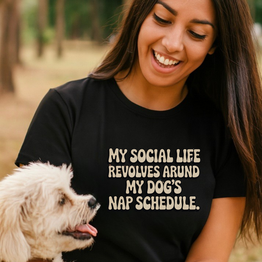 Woman wearing a black t-shirt with a humorous dog quote, sitting outdoors with a small white dog.