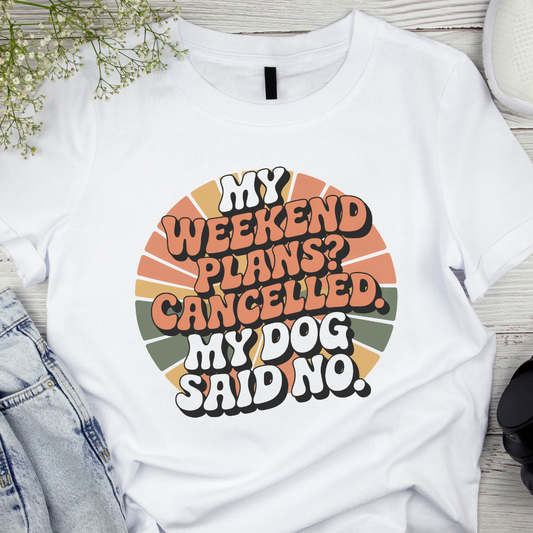 White t-shirt with colorful text design on a wooden surface with denim jeans and flowers.
