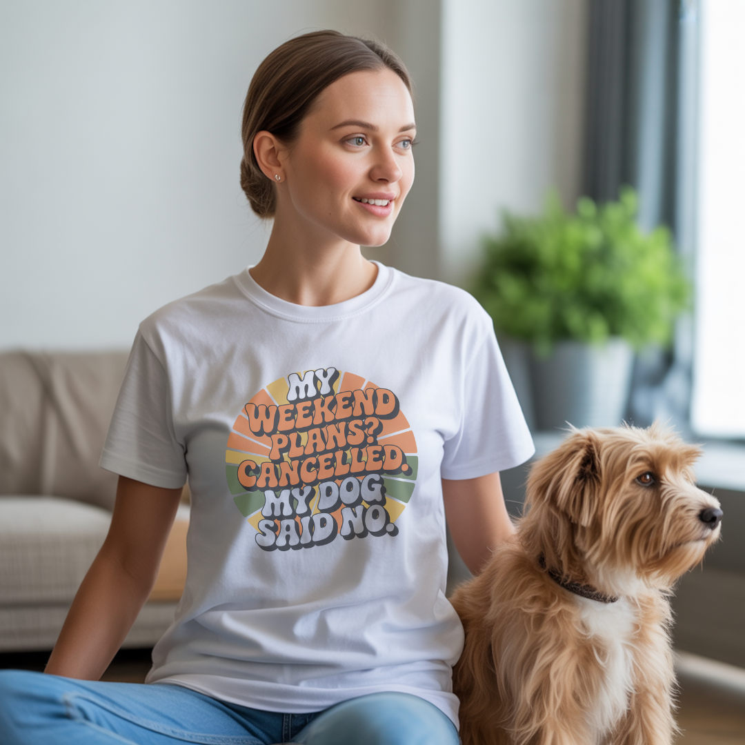 Woman wearing a white t-shirt with a humorous dog-themed design, sitting with a dog in a living room.