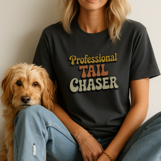 Person wearing a black t-shirt with 'Professional Tail Chaser' text sitting next to a dog.